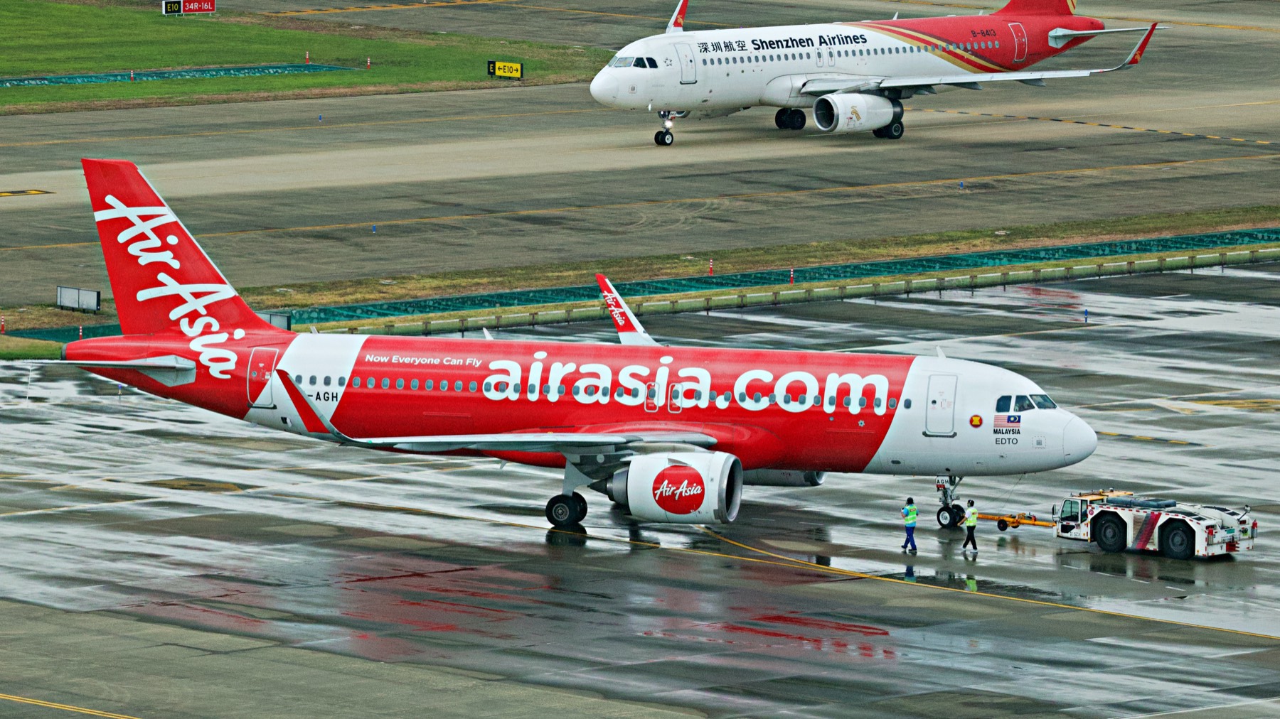 雨后的机坪。AirAsia 推出,深航滑行经过,两个地勤跟着牵引车走在湿漉漉的反光里。